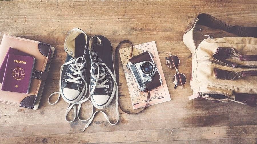 Pasaporte, cámara, gafas y equipaje preparados sobre una mesa antes de un viaje